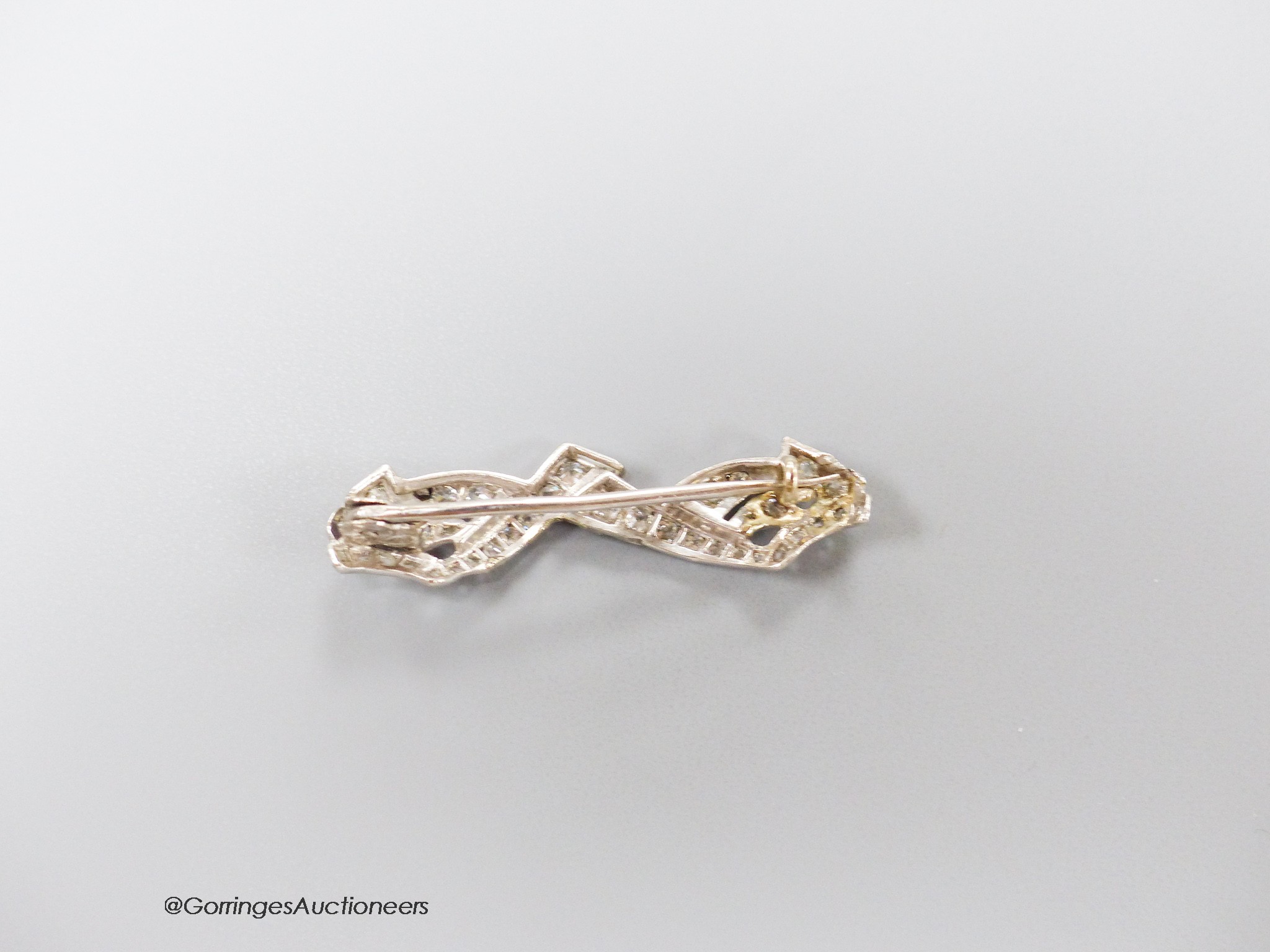 A white metal and diamond cluster set shaped bar brooch, 38mm, gross weight 4 grams.